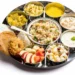 alt="Gujarati Farali Thali for Shravan featuring Sabudana Khichdi, Sabudana Vada, Rajgira Puri, Kheer, and fresh fruit slices"